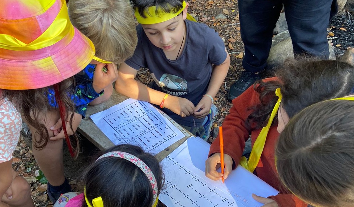 Estudiantes resolviendo un desafío de códigos en una mesa al aire libre