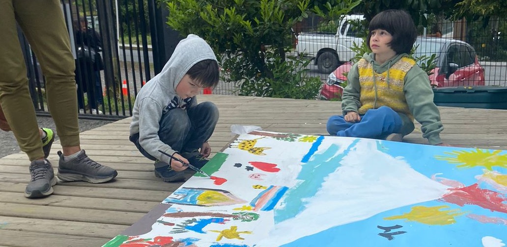 Dos niños pintando un mural con el volcán en una terraza de madera